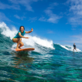 white woman on surfboard riding a wave under a beautiful blue sky